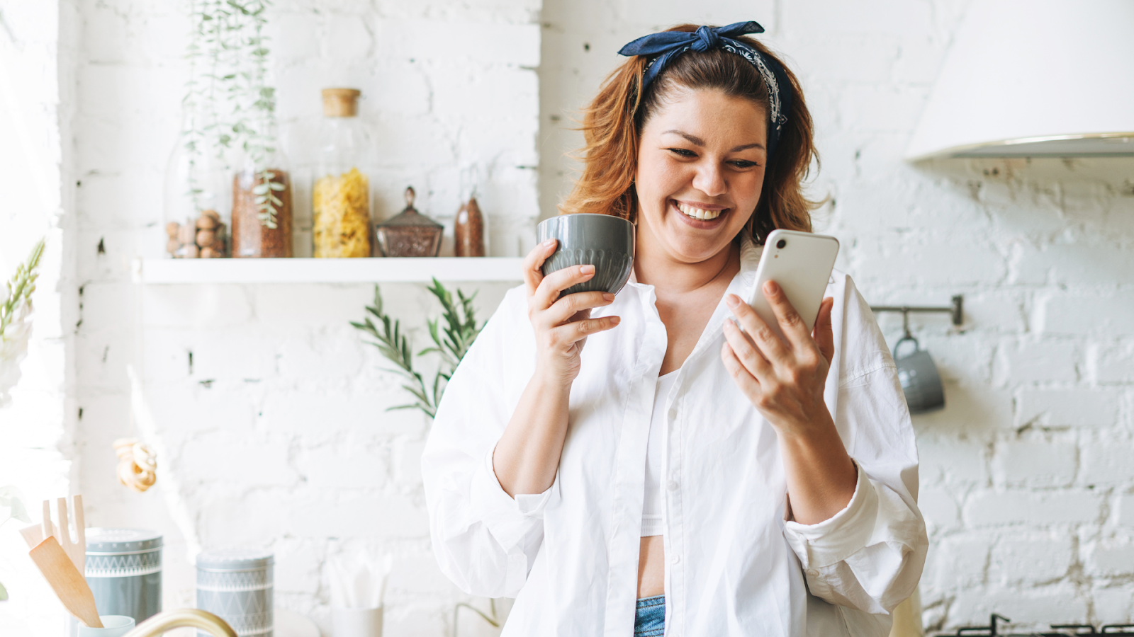 A Woman looking at her phone smiling with a cup of coffee.