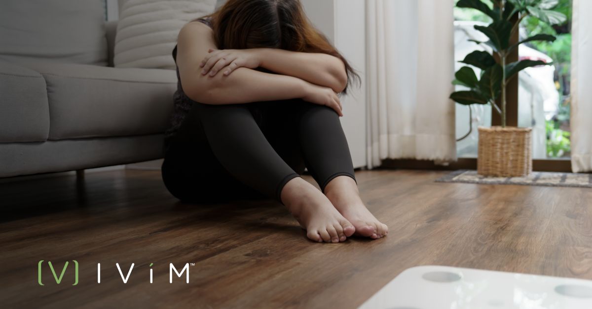 Woman looking exhausted from a weight loss plateau, sitting on the floor, symbolizing the emotional struggle during a weight loss journey.
