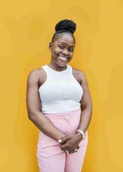 Ivim Health patient Gbemisola Ogun smiling in white top and pink pants against yellow background after 42-pound weight loss